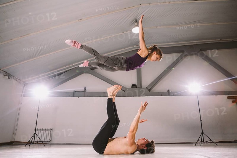 Young couple Couple practicing acro yoga in gym. Healthy lifestyle. Acroyoga. Couple yoga. Partner yoga. Muscular man throwing women to air. Concept of trust, strength and courage