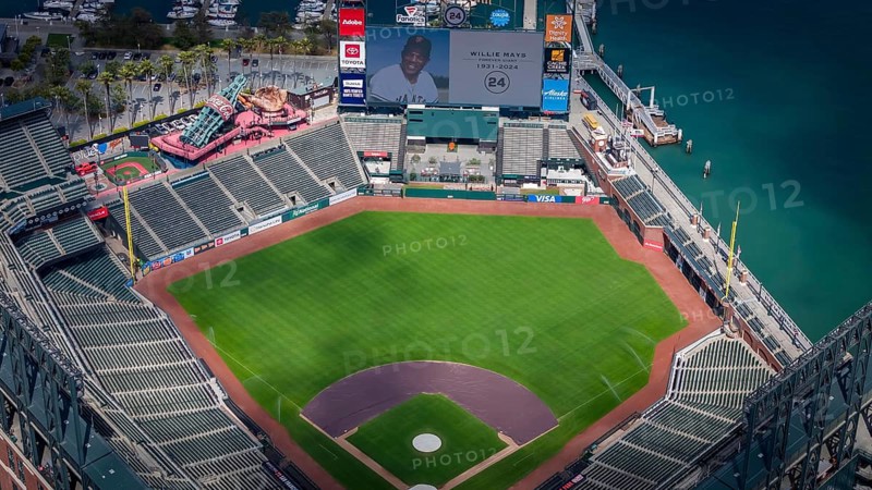 The San Francisco Giants honor Willie Mays, who recently passed away, with a tribute on the centerfield Jumbotron at Oracle Park. The aerial view captures the stadium's beauty against the backdrop of San Francisco Bay