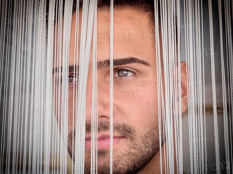Headshot of handsome young man behind strings curtain, looking away to a side