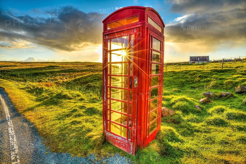Urban red telephone box in the middle of a green countryside. Concept for synergy between modern and rural area. Red and green complementary colors join together in a scottish land, United Kingdom