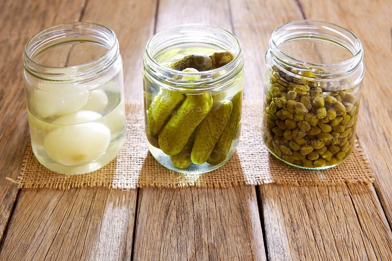 Bottled pickles as capers onion and cucumbers in wooden table