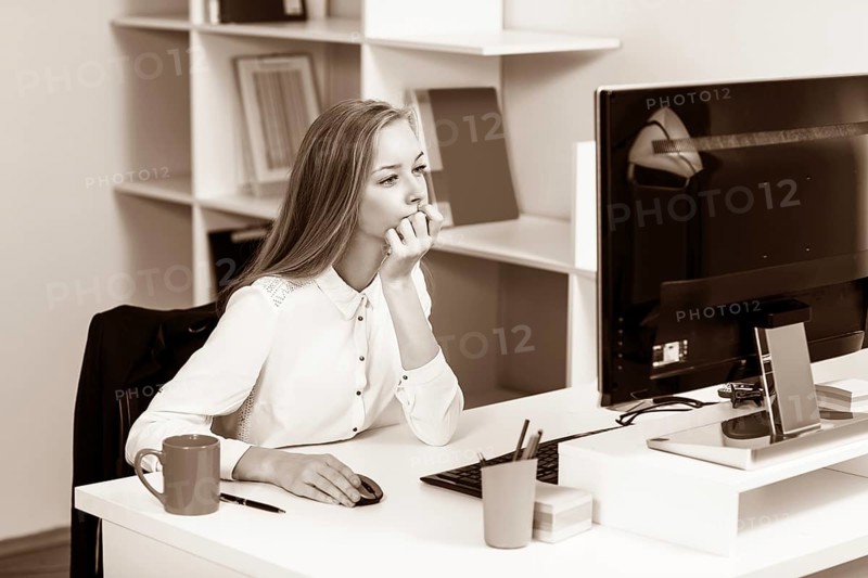 Young pretty business woman sitting at the desk with computer in blue office