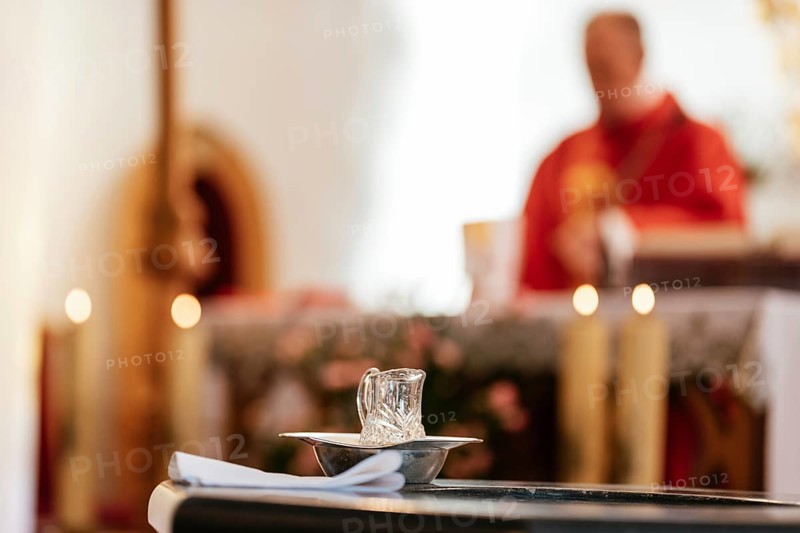 Holy water during baptism catholic mass with priest in the background