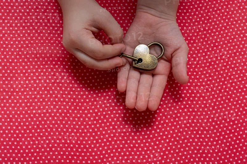 Hand holding a heart shaped lock and key on a red background