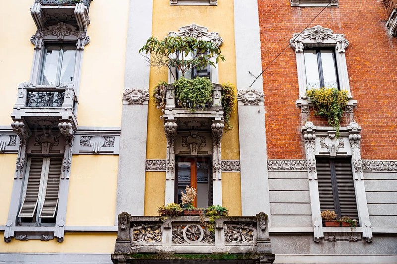 Facade of the building with stucco, balconies and flowerpots. Milan, Italy.