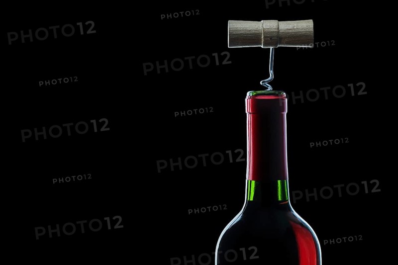 Corckscrew in bottle of red wine on black background