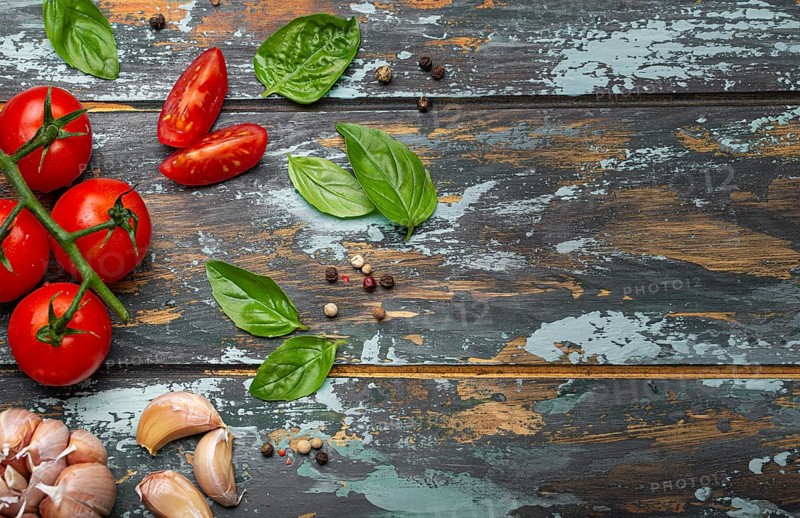 Food cooking border with cherry tomatoes, fresh green basil and garlic cloves top view on rustic colourful wooden background, ingredients for preparing meal, copy space, food photography, food photography
