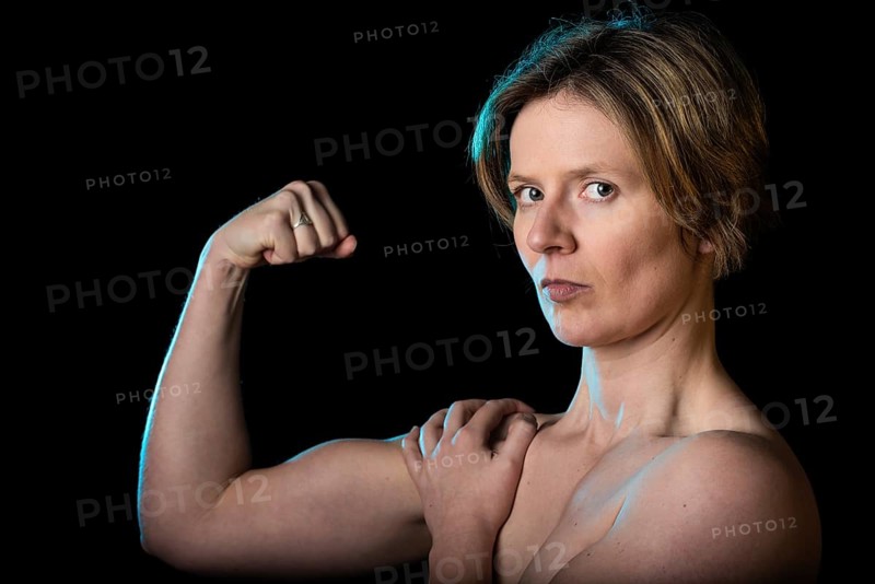Low key studio portrait of a 35 year old white woman with naked shoulders showing her biceps, Brussels