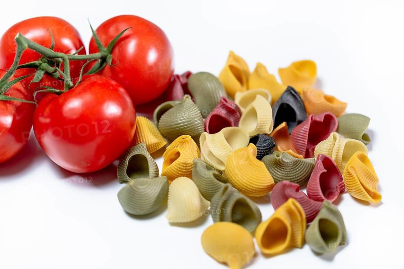 Coloured Italian snail pasta made from durum wheat semolina with red vine tomatoes against a white background