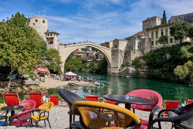 Cafe with colourful chairs on the bank of the river Neretva, behind the bridge Stari Most, numerous tourists, old town of Mostar, Bosnia-Herzegovina