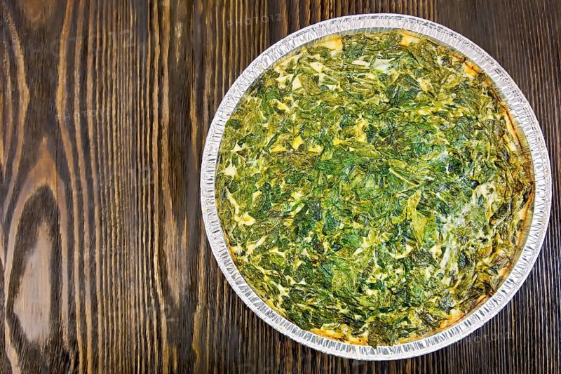 Celtic cake with spinach, tomatoes, oatmeal and eggs in baking dish from a foil against the backdrop of wooden planks on top