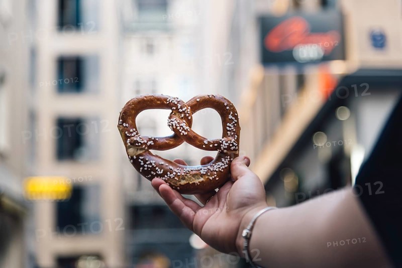 Woman hand holding a pretzel against cityscape. Focus on bread, blurred background