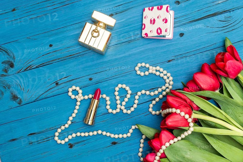 Red tulips in the necklace, lipstick and bottle of perfume on the background of blue wooden board
