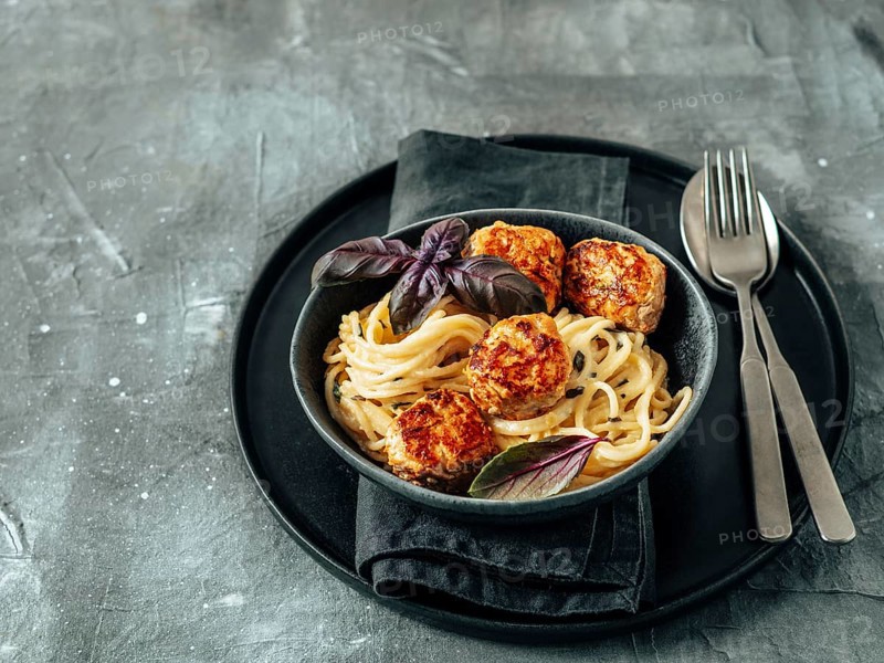 Zucchini Parmesan Meatballs with Pasta Carbonara in black craft plate over gray background. Close up view of creamy carbonara with copy space left