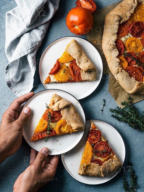 Savory fresh homemade tomato tart or galette.Hands takes piece of pie.Ideas and recipes healthy lunch, appetiezer-whole wheat or rye-wheat pie with tomatoes, cheese.Harvest tomatoes.Top view.Vertical