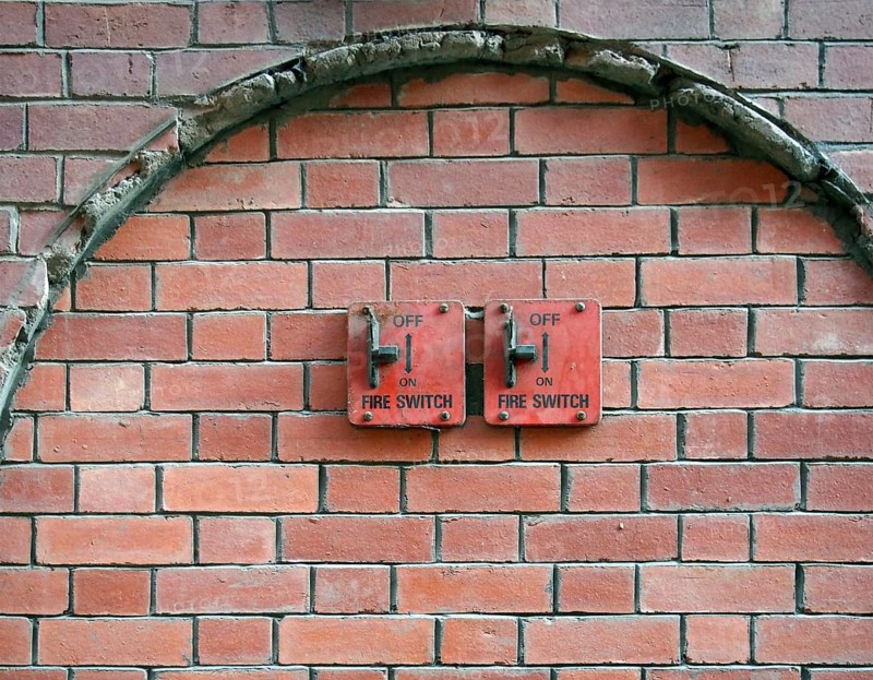 Two old red metal fire switches on an exterior brick wall