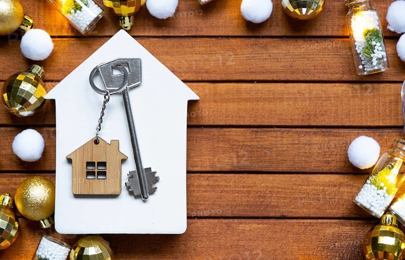 Key to house with a keychain tiny home on wooden background with Christmas decor layout. Gift for New Year, Christmas. Building, project, moving to new house, mortgage, rent and purchase real estate