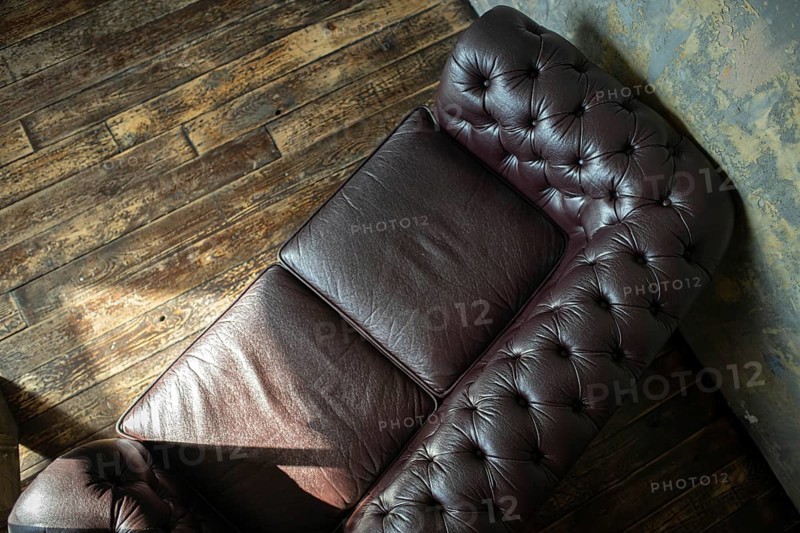 Top view of a vintage tufted leather couch against a wooden floor and textured wall