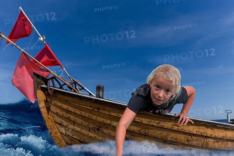 Child in a wooden boat with waves and holding his hand in the water