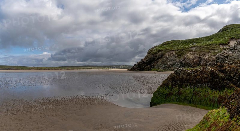 View of the picturesque golden sand Maghera Beach with algae-covered rocks and cliffs in the foreground