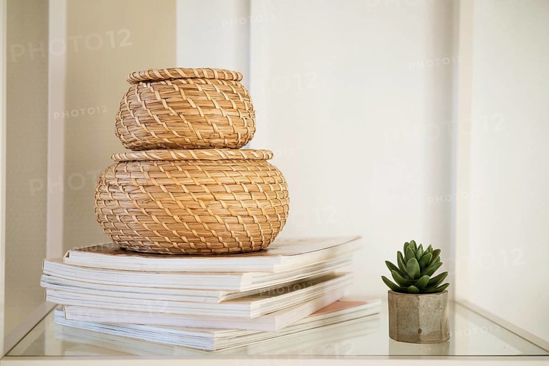 Close-up of a round straw box with a lid on a white shelf. Eco-friendly items for storing small items, organising space. Home decor decorative items. Stand on a shelf in the room