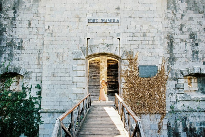 Groom hugging bride behind the half-opened door of Mamula Fort.