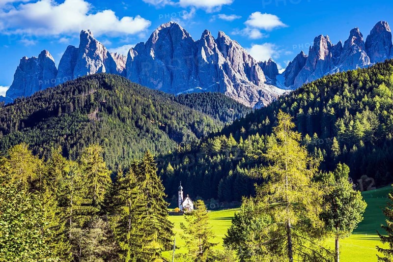 Dolomites, Tirol. Sunny warm autumn day. Rocky peaks and forested mountains surrounded by green Alpine meadows. The symbol of the valley Val di Funes - church of Santa Maddalena