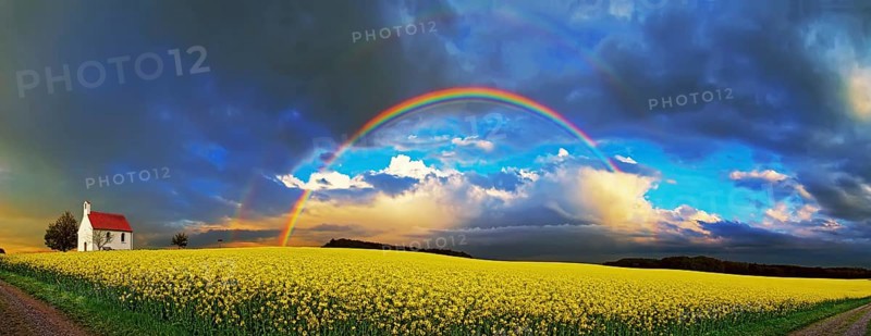 Panorama, chapel and rainbow over a rapeseed field
