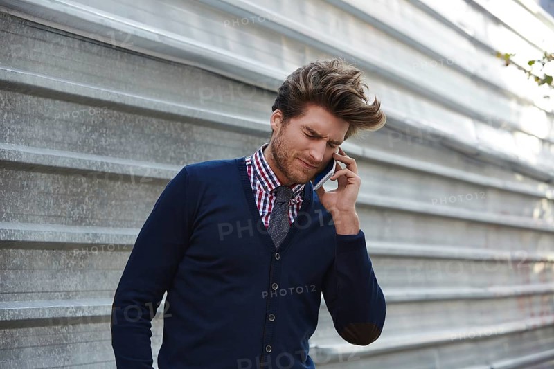 Young businessman talking smartphone phone on the street metal fence