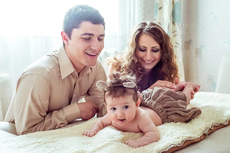 Naked baby with her parents lying on soft blanket in the room