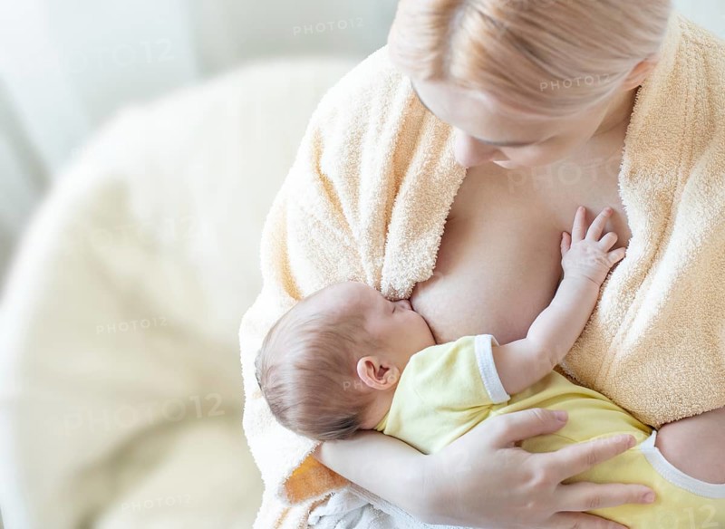 Baby eating breast milk. Caucasian blonde young mother breastfeeding her baby horizontal photo. Concept of lactation