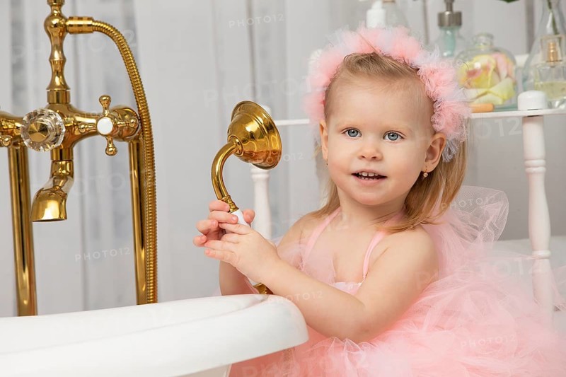 Little funny girl in a smart pink dress in the bathroom