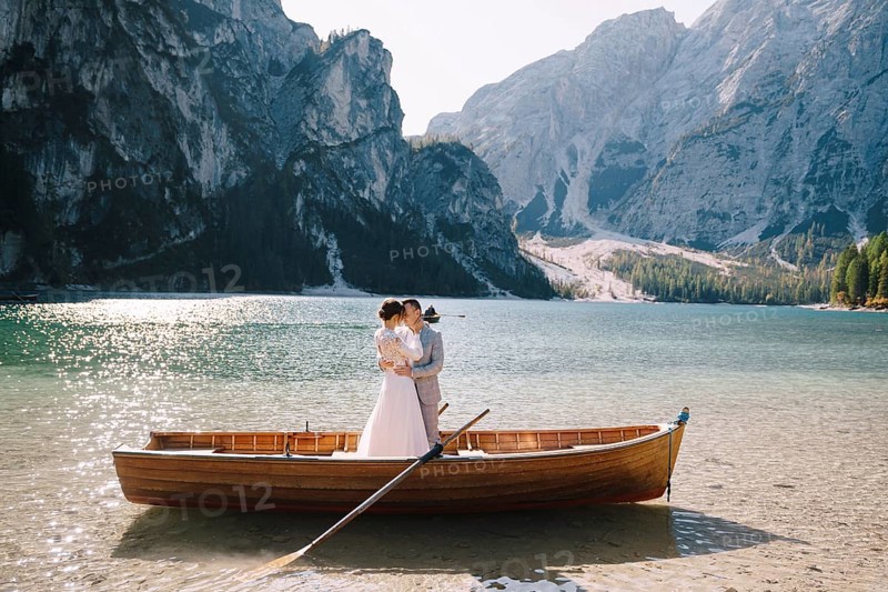 Bride and groom sailing in wooden boat, with oars at Lago di Braies lake in Italy. Wedding in Europe - Newlyweds are standing embracing in a boat