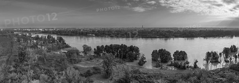 Cremona, Italy, October 20th 2024 Aerial view of a river overflowing its banks, flooding the surrounding trees and fields, with a city skyline in the background