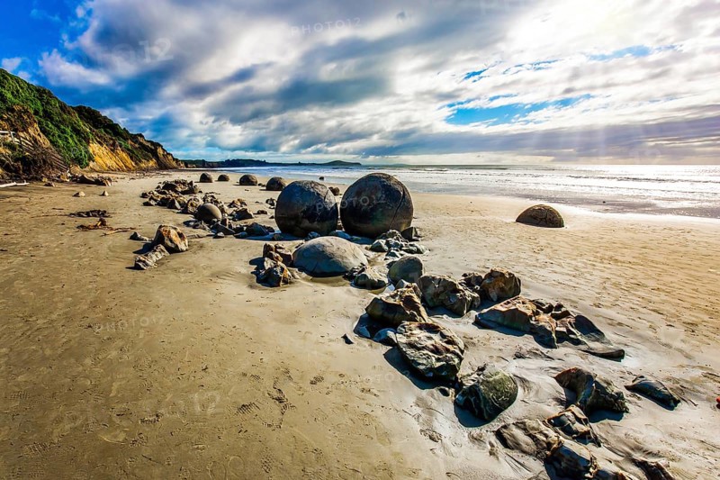 Sunny day on the beach. Low tide in the Pacific. Series of mysterious round boulders Moeraki and their shattered remnants on a sandy beach. New Zealand. The concept of exotic and ecological tourism