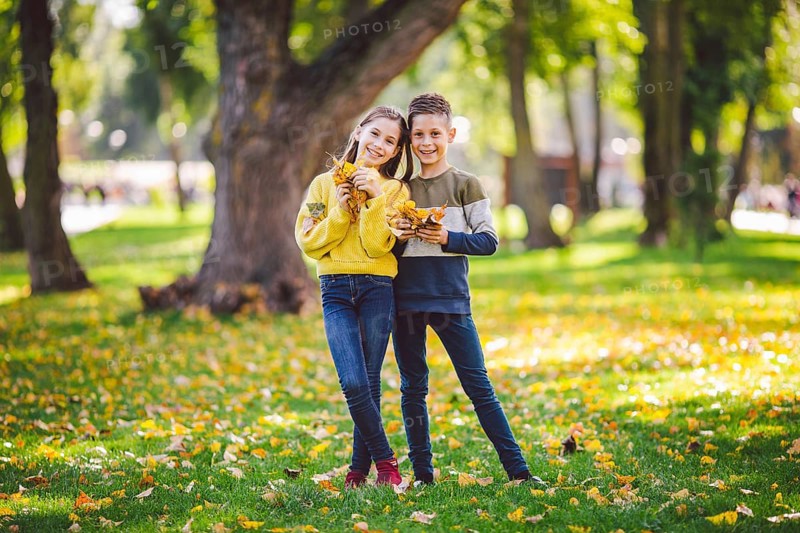 Friendship between siblings. Siblings together outside with bright coloured background. Kids autumn portrait. Brother and sister playing in autumn park leaves. Family active fall weekend concept