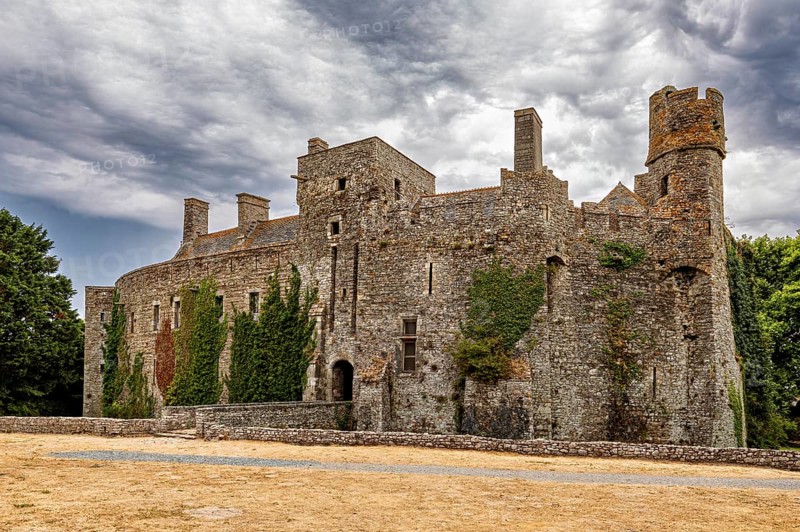 Stone castle with towers and ivy in front of a cloudy sky, Pirou Castle in Normandy, France