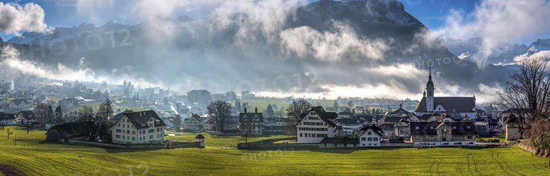 Panorama over the village of Schwyz, Switzerland with wisps of fog and clouds in oblique sunlight, Schwyz, Switzerland