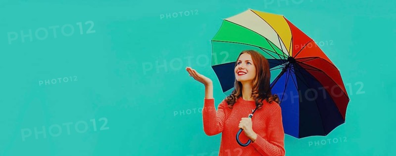 Autumn portrait of happy smiling young woman holding colorful umbrella wearing red knitted sweater on blue background