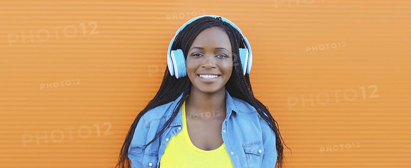 Portrait of happy African young woman listening to music with headphones, cool modern black teenage girl smiles on colorful bright orange background, summer day