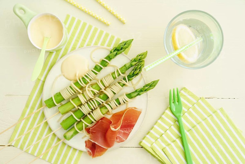 Steamed green asparagus on wooden skewers with spaghetti wrapped in hollandaise sauce and ham