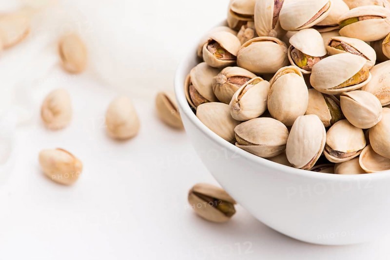 Bowl of roasted pistachios on a white background
