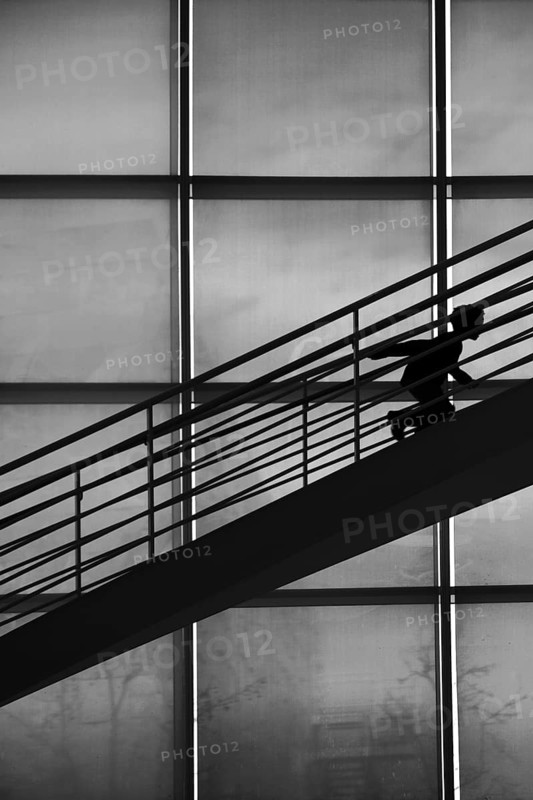 The silhouette of a boy climbing a staircase in a stooped posture