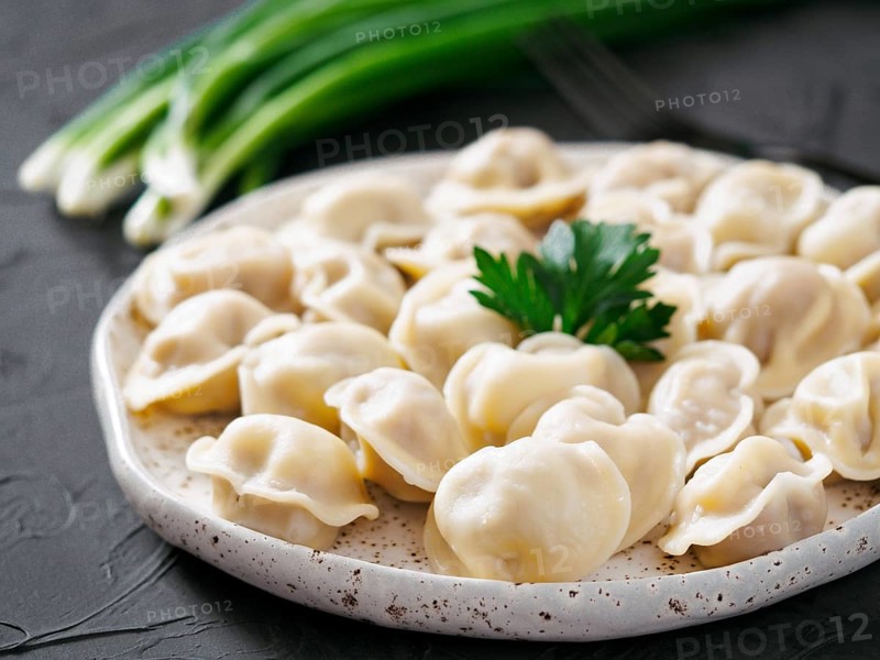 Traditional russian pelmeni, ravioli, dumplings with meat on black concrete background. Russian food and russian kitchen concept