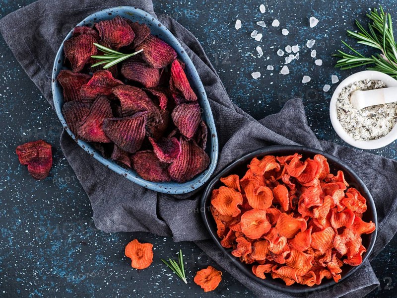 Baked beet and carrot slices with coarse sea salt scented rosemary. Vegan diet food idea and recipe. Healthy homemade beetroot and carrot chips in plate and ingredients on dark blue background. Copy space. Top view