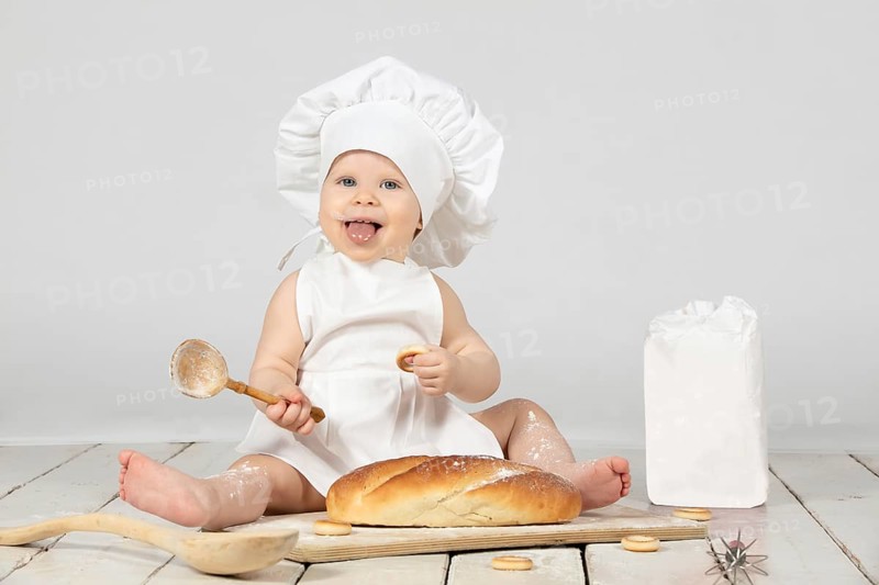 Child cooking. Beautiful little girl in cooking clothes with a long loaf of bread and flour. The child is one year old. Funny baby laughs. Little cook. The concept of baking bakery products