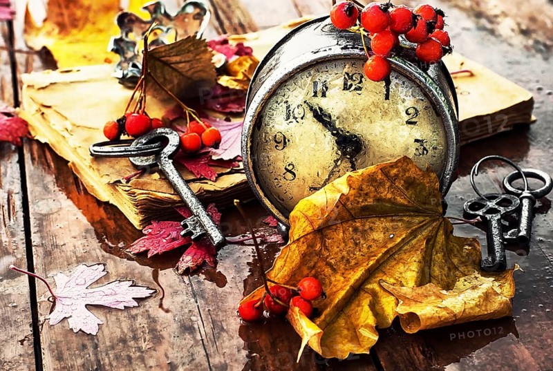Od clock book and the keys on the wet table strewn with autumn leaves.Photo tinted