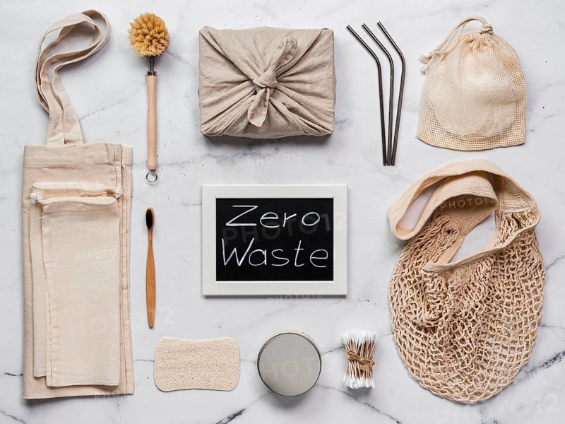 Zero waste concept. Textile wrapping gift, eco bags, metal straws, eco-friendly kitchen tools, bamboo toothbrush and cotton buds, reusable cotton pads on white marble background. Top view or flat lay
