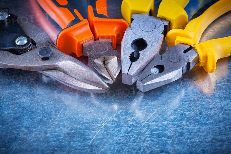 Close up view of tin snips gripping tongs nippers on scratched vintage metallic surface construction concept