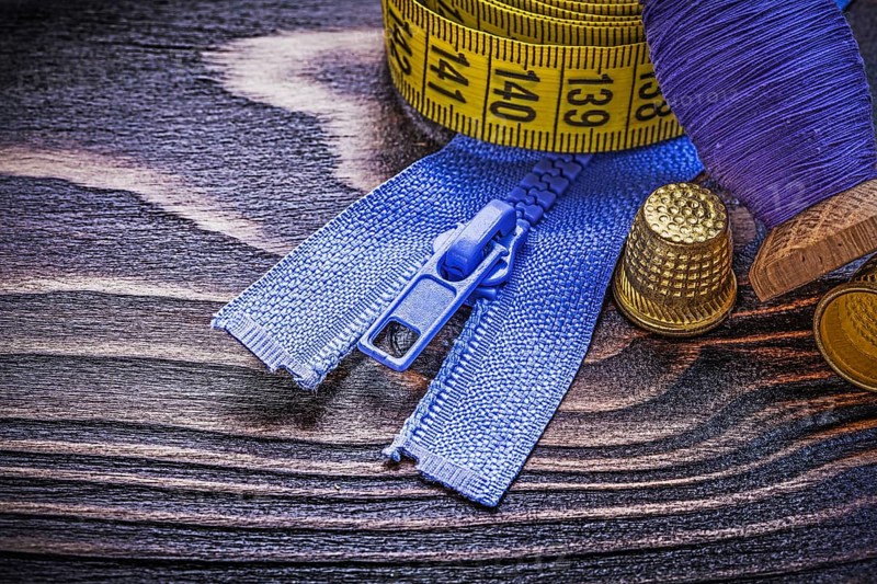 Vintage spool of thread measuring tape thimbles zip fastener on wooden board needlework concept